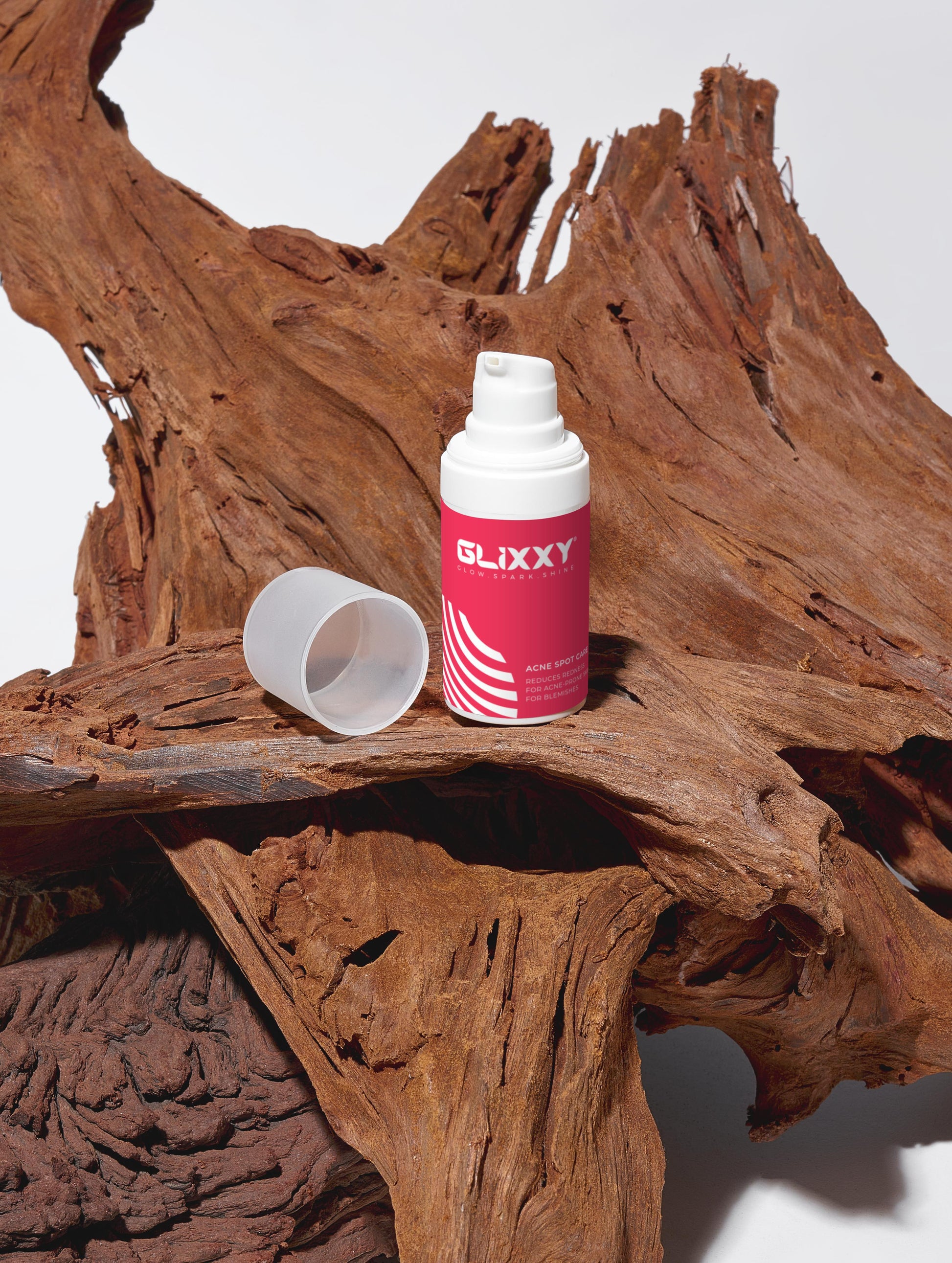 Glixxy acne spot cream bottle and cup on a wooden surface