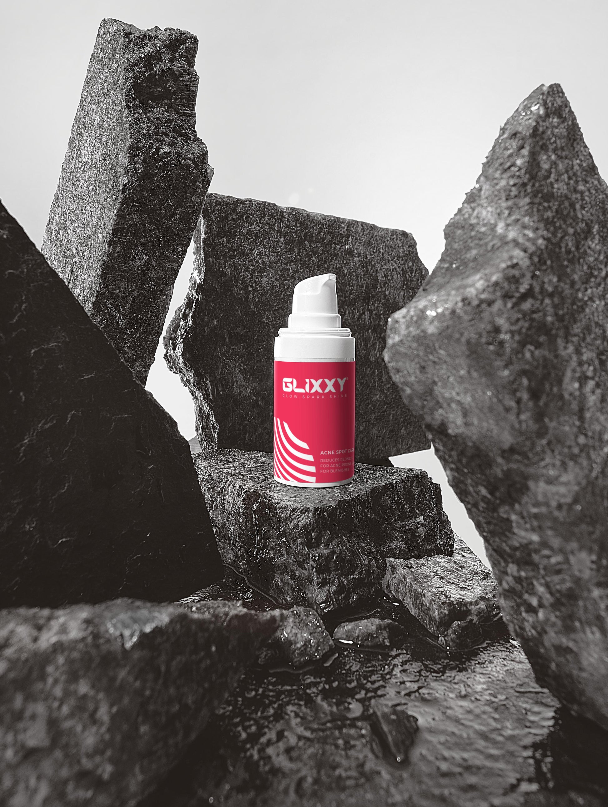 Red and white canister of acne spot cream labeled 'Glixxy' on a black stone surface