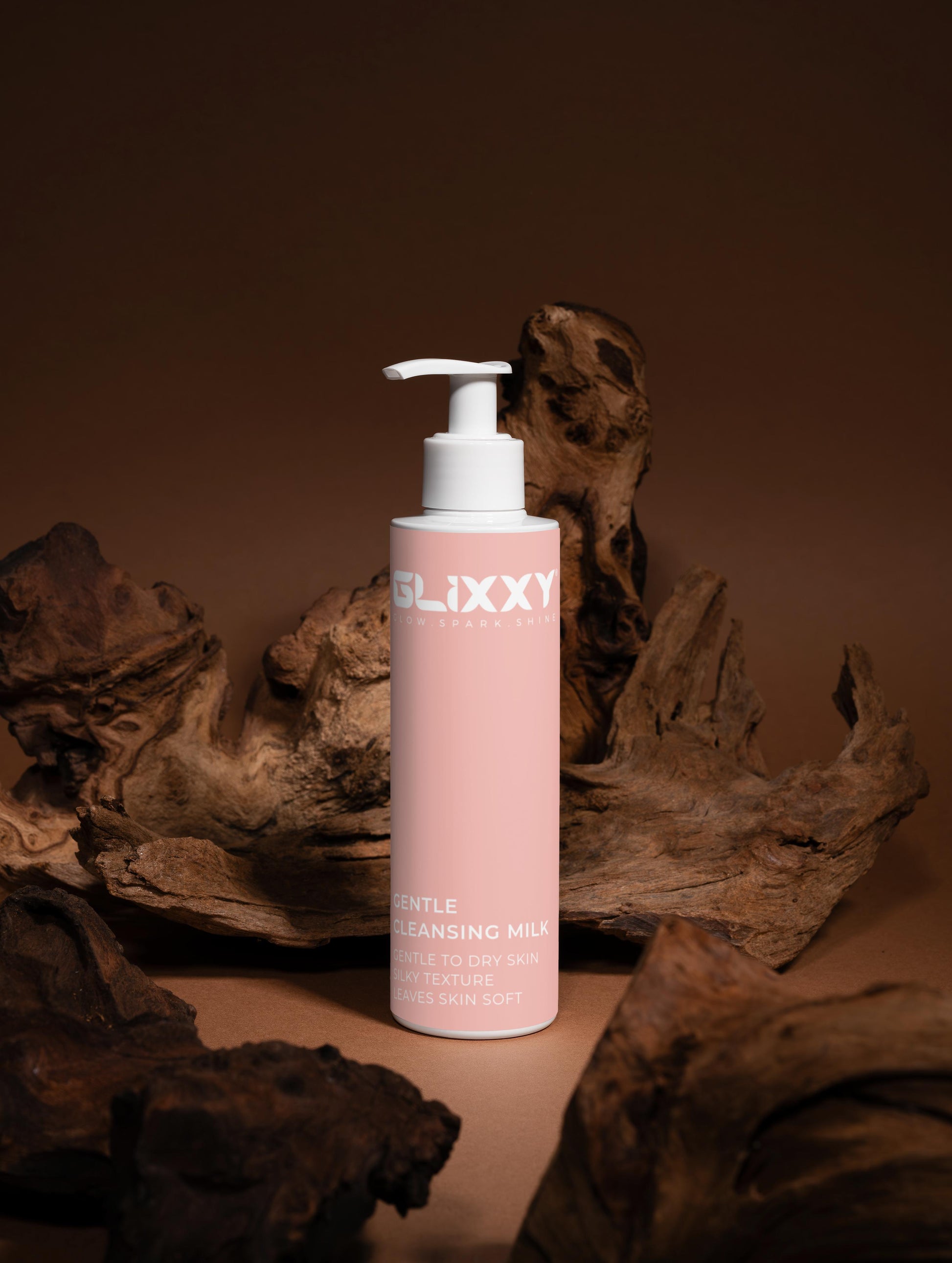 Pink bottle of Glixxy Gentle Cleansing Milk against a brown background with natural elements.