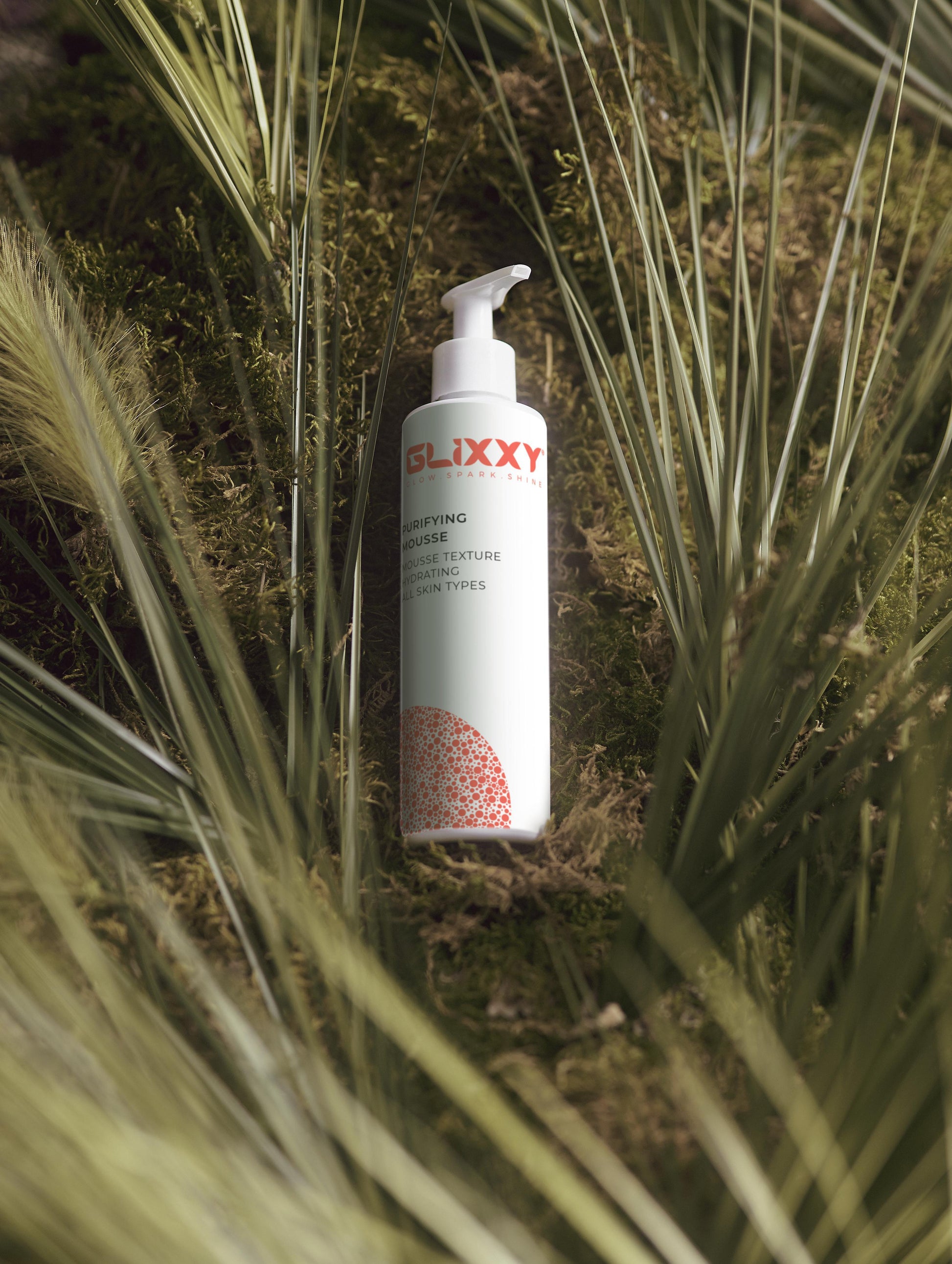 Glixxy purifying mousse bottle in a natural setting with grass and moss
