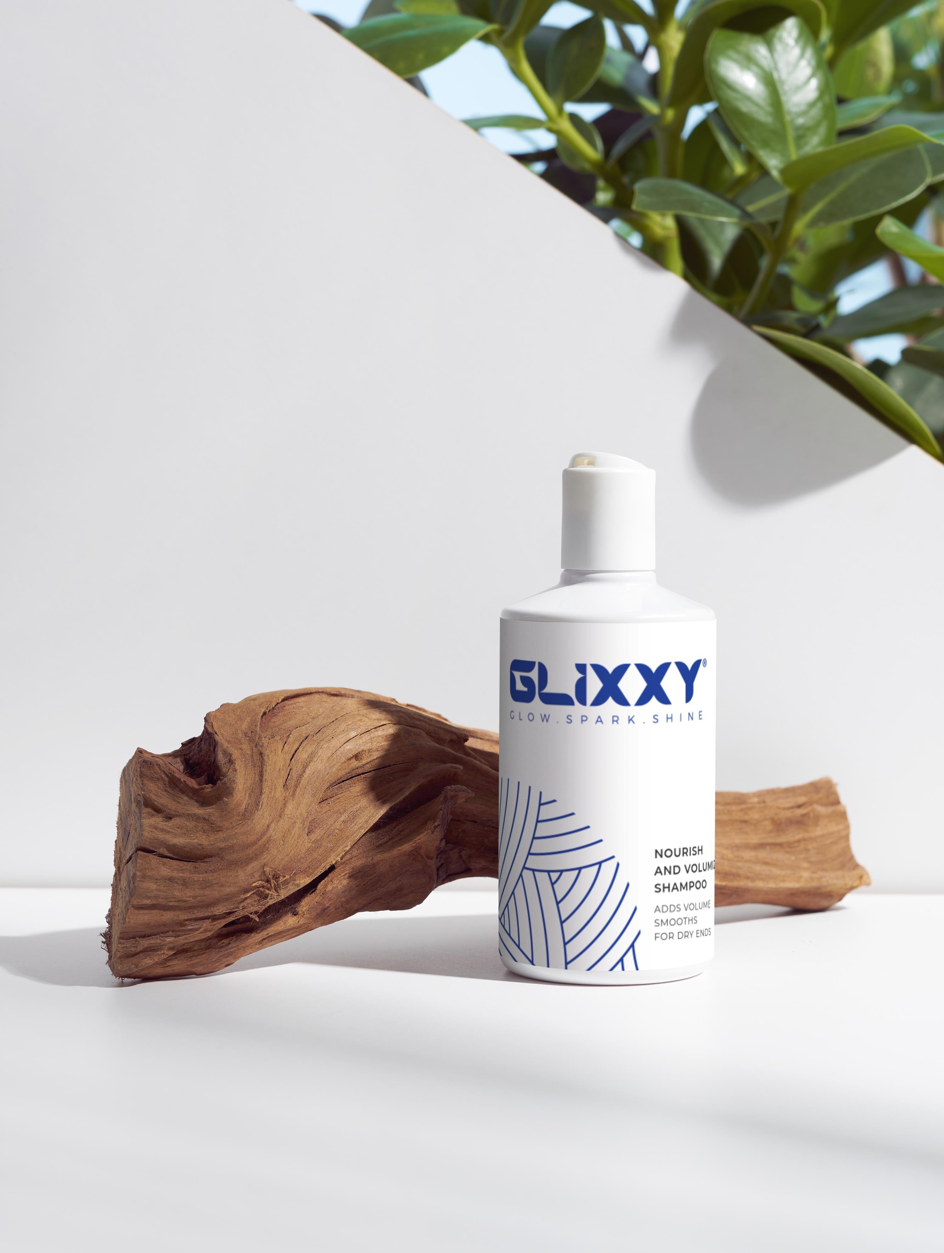 Glixxy best volumizing shampoo bottle on a white surface with a wooden log and plant in the background