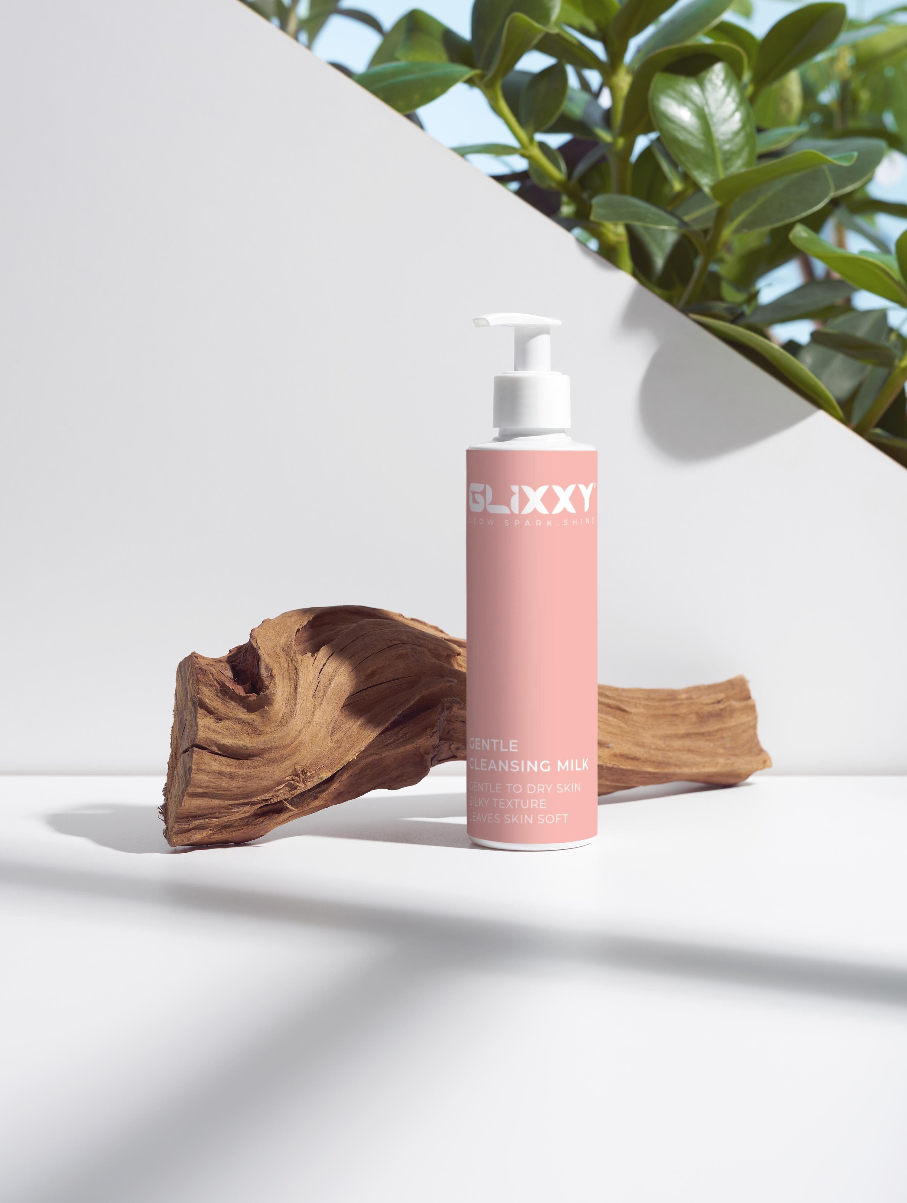 Pink bottle of GLIXXY product on a white surface with a plant in the background