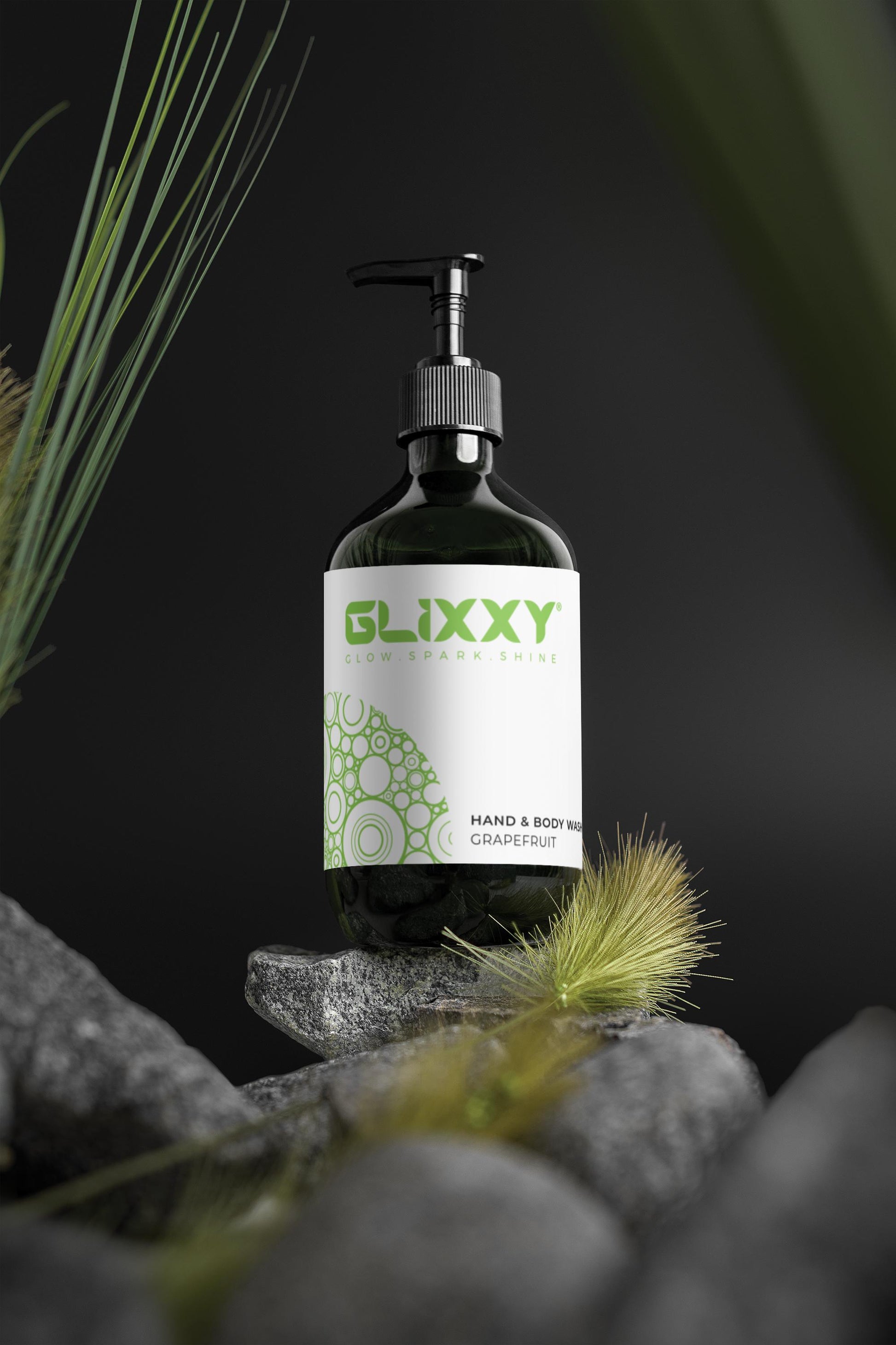 Glixxy hand and body wash bottle on a dark background with greenery